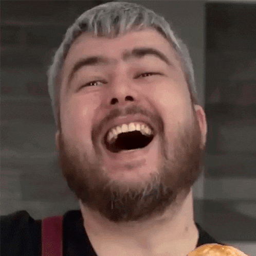 a man with a beard is laughing while holding a pizza .