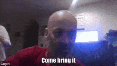a bald man with a mustache is talking on a video call and says come bring it .