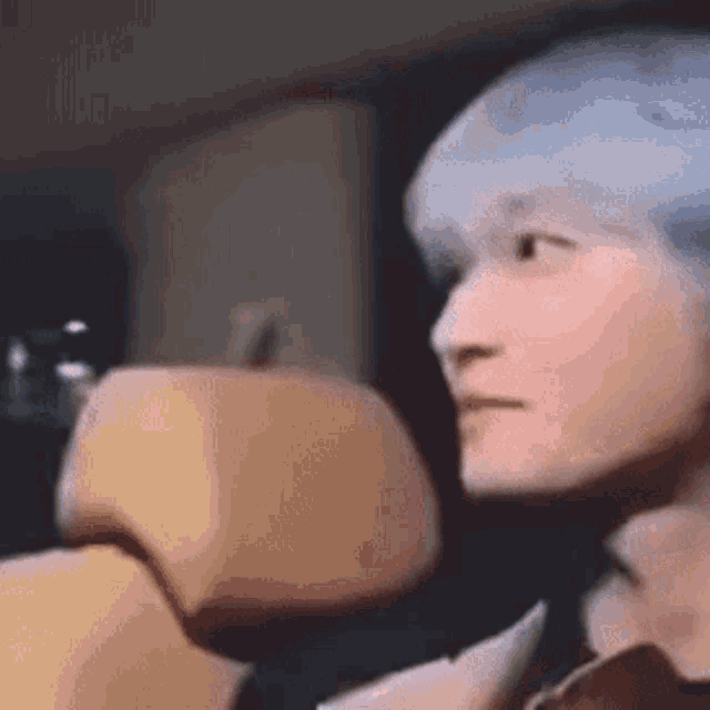 a man with blue hair is sitting in the back seat of a car and looking at something .