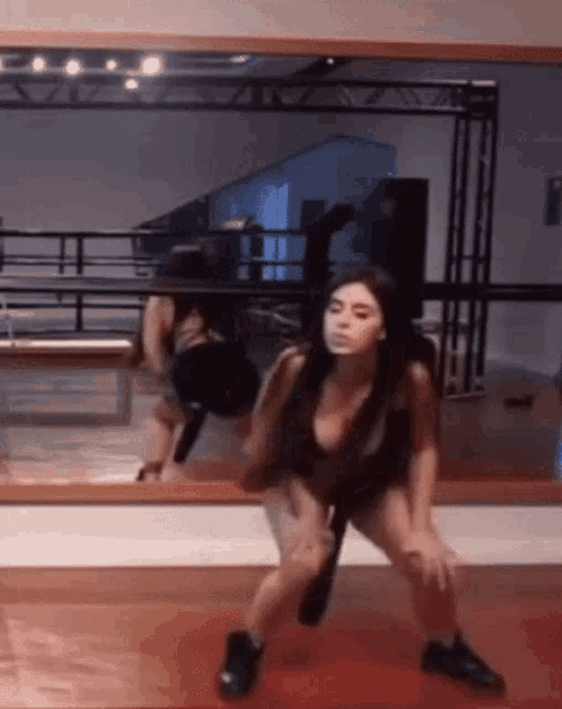 a woman is dancing in front of a large mirror in a gym .