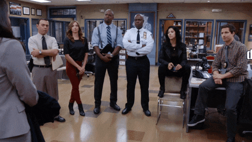 a group of police officers stand in a room with a woman standing in front of them