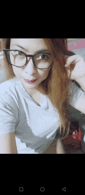 a woman wearing glasses and a gray shirt is taking a selfie