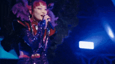 a woman in a purple costume is singing into a microphone on a stage .