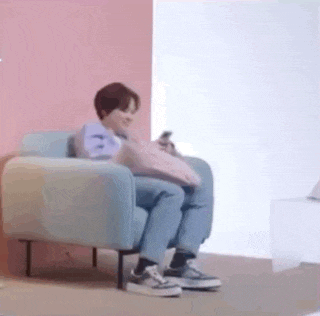 a person is sitting in a chair holding a pillow and looking at a cell phone .