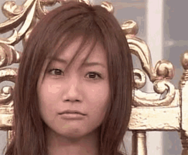 a woman is sitting in a chair with a gold throne in the background and making a funny face .
