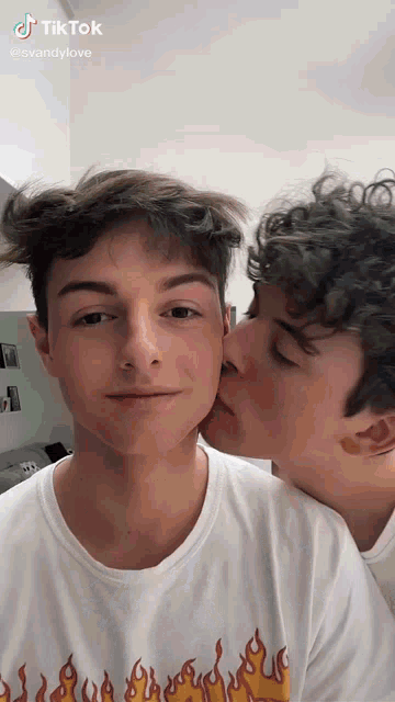 a man is kissing another man on the cheek while wearing a shirt with flames on it .