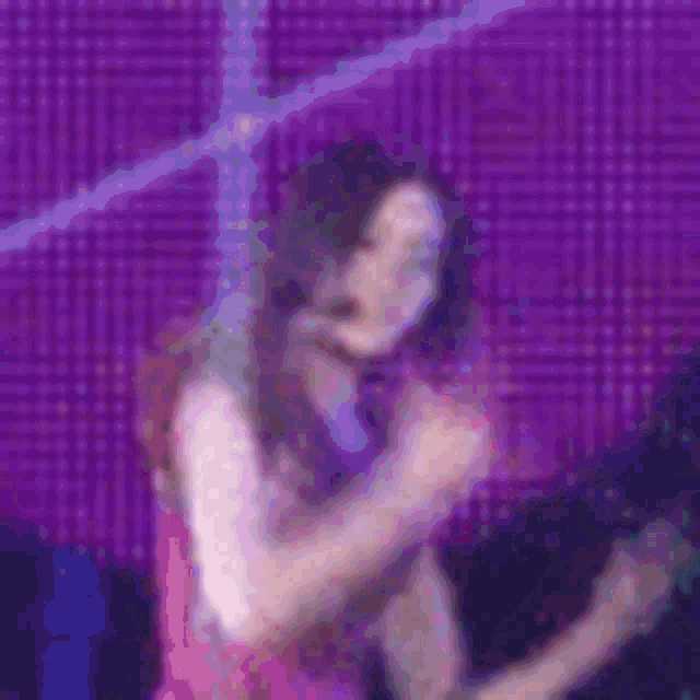 a woman in a pink dress is singing into a microphone on a stage in front of a purple background .