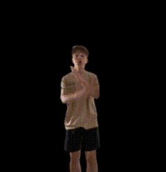 a boy is standing in front of a black background and covering his mouth with his hand ..