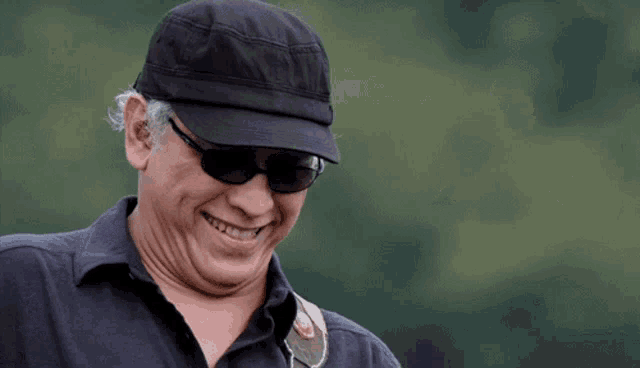 a man wearing a hat and sunglasses looks down at something