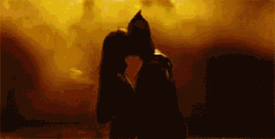 a man and a woman are kissing in front of a fire in a dark room .