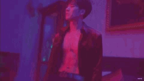 a man without a shirt is taking a shower in a pink and purple light .