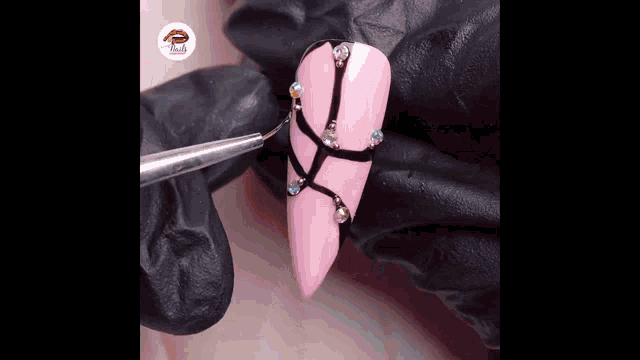 a person is applying nail polish to a pink nail with rhinestones and a brush .