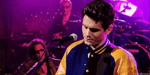 a man in a yellow and blue jacket is singing into a microphone while playing a guitar .