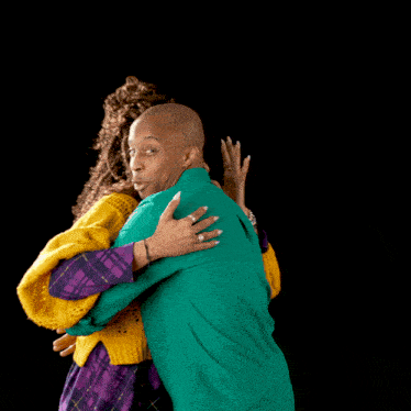 a man in a green shirt and a woman in a yellow sweater hugging each other