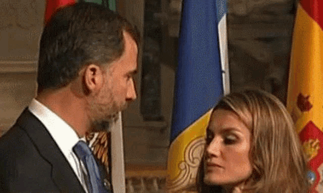 a man in a suit and tie is looking at a woman in front of flags .