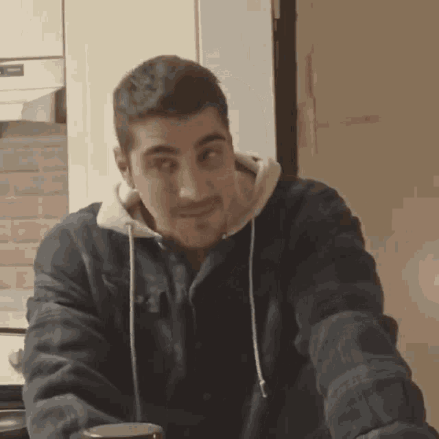 a man wearing a blue jacket with a white hood is sitting in a kitchen