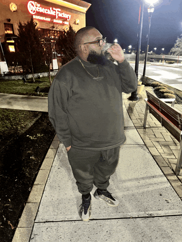 a man drinks from a cup in front of the cheesecake factory