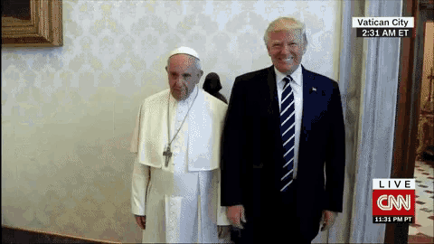 a man in a suit and tie stands next to a man in a white robe in front of a cnn live broadcast