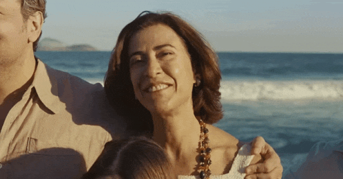 a woman wearing a necklace smiles while standing on a beach