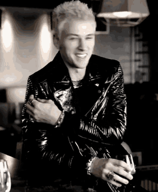 a man in a black leather jacket is smiling while holding a glass of wine