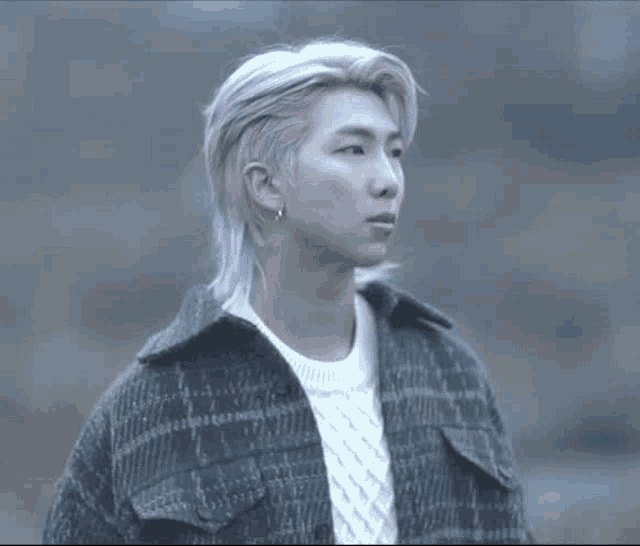 a man with long blonde hair is wearing a plaid jacket and a white sweater .