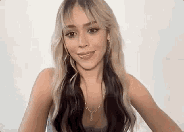 a woman with blonde and black hair is wearing a necklace and smiling at the camera .