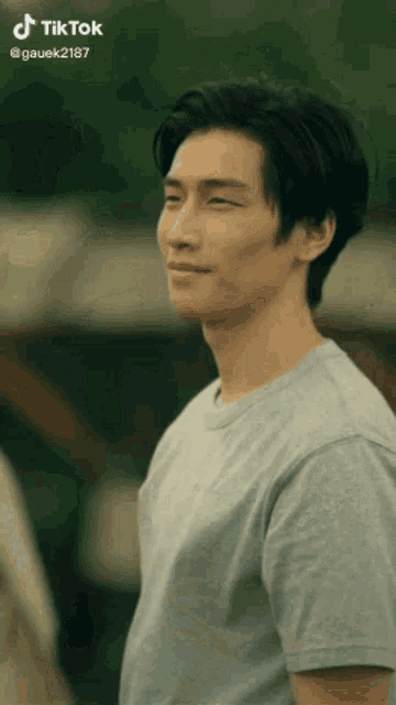 a man in a grey t-shirt is smiling and looking at the camera .
