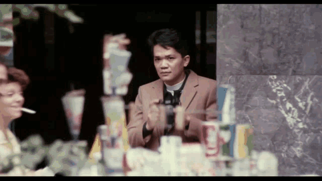 a man in a brown suit stands in front of a stack of soda cans that say sprite