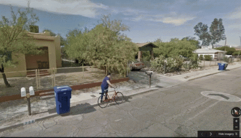 a person riding a bike on a sidewalk next to a blue garbage can