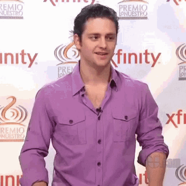 a man in a purple shirt stands in front of a wall that says finity