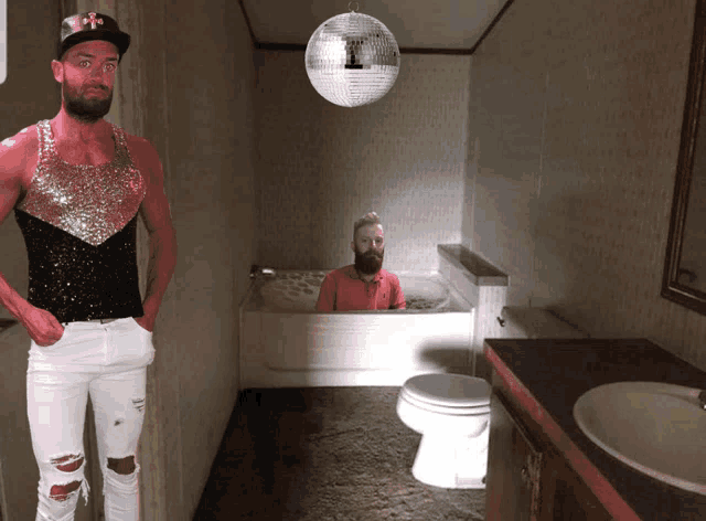 a man standing next to a man in a bathtub with a disco ball hanging from the ceiling