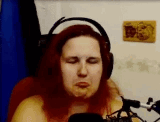 a woman with red hair is wearing headphones and making a funny face while sitting in front of a microphone .