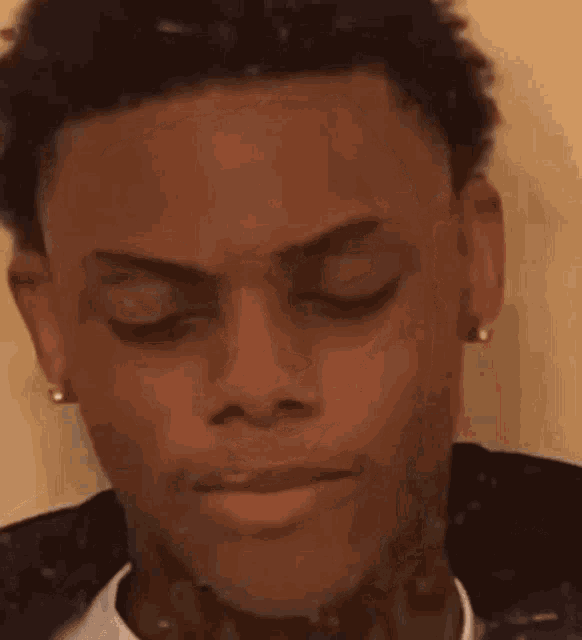 a close up of a young man 's face with his eyes closed and a tattoo on his neck .