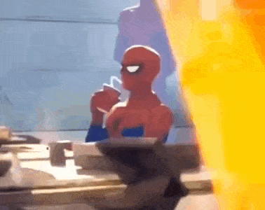 a man in a spiderman costume is sitting at a table drinking from a cup .