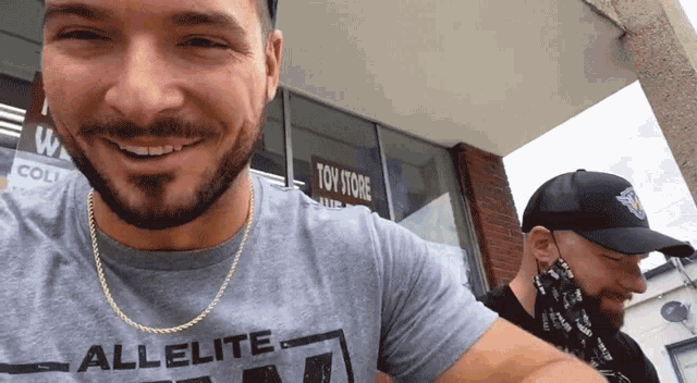 a man wearing an all elite t-shirt is smiling in front of a toy store