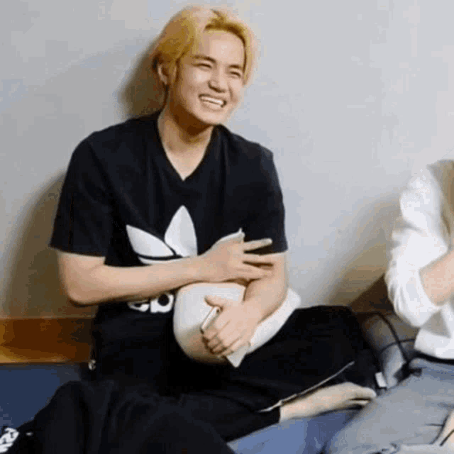 a man is sitting on a bed with a pillow in his lap and laughing .