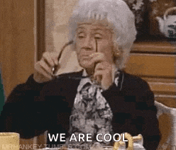 an elderly woman is sitting at a table holding a pair of glasses and says `` we are cool '' .