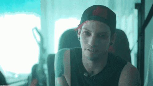 a young man wearing a hat and a black tank top is sitting in a chair .