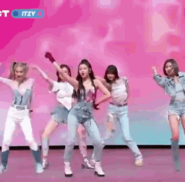 a group of women are dancing on a stage in front of a pink wall .