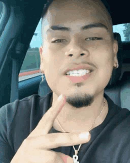 a man with braces on his teeth is sitting in the back seat of a car giving a peace sign .