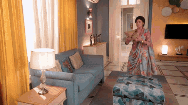 a woman in a sari stands in a living room with a blue couch