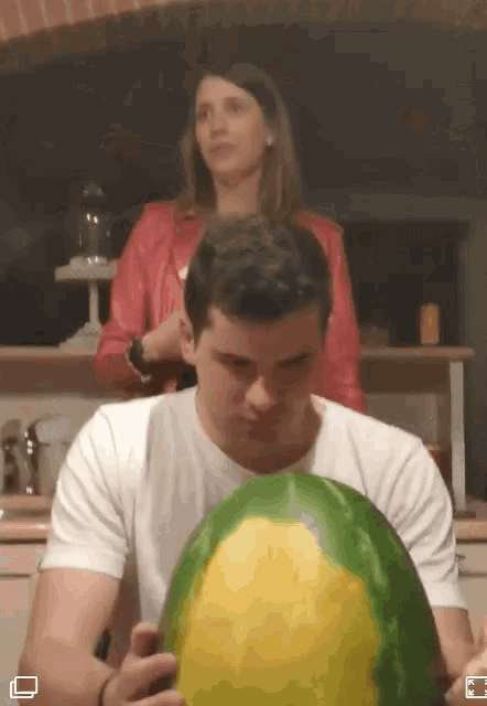 a man is holding a watermelon in front of a woman in a red jacket