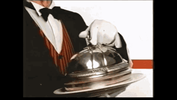 a man in a tuxedo holding a silver dome