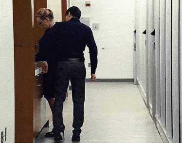 a man and a woman are walking down a hallway with a fire extinguisher on the wall