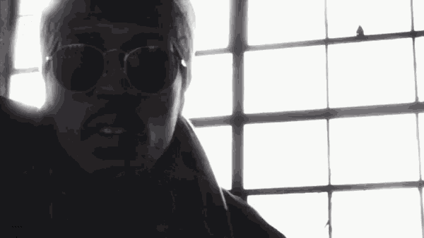 a man wearing sunglasses and a bandana is standing in front of a window