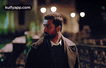 a man with a beard is walking down a street at night and looking at the camera .