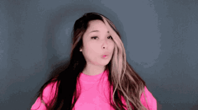 a woman with long hair wearing a pink shirt blows a kiss