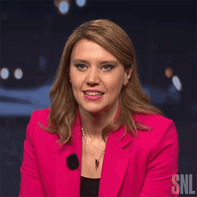 a woman wearing a pink jacket with the snl logo on the bottom