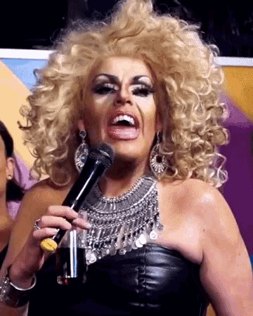 a woman with blonde curly hair is holding a microphone and a glass