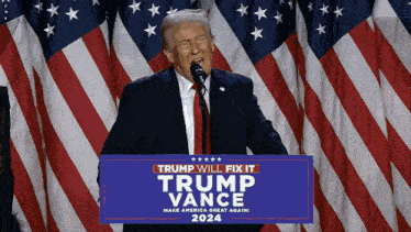 a man stands at a podium with a sign that says trump will fix it trump vance